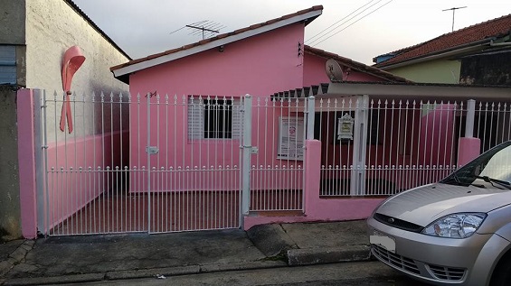 Casa toda pintada em rosa, com um laço da mesma cor, na parede lateral do prédio vizinho, símbolo da ONG. 
